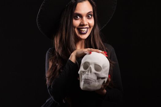 Beautiful brunette woman dressed up like a scary witch holding a human skull