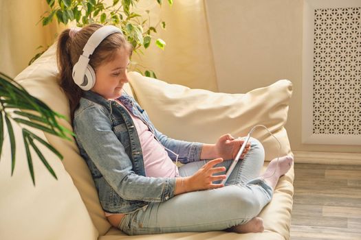 Cute little girl in casual clothes and headphones using a tablet