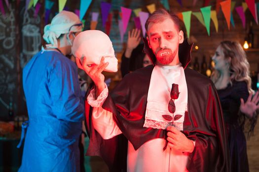 Count dracula holding a human skull and looking into the camera at halloween celebration