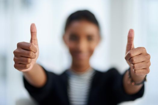Business is booming. Defocused shot of a young businesswoman posing with her thumbs up at work.