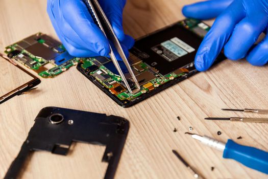 The technician repairing the smartphone's motherboard in the workshop on the table.