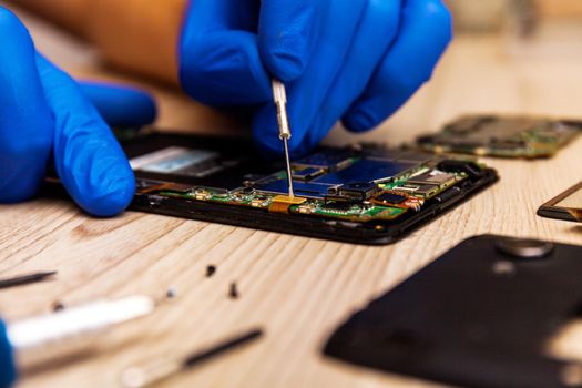 The technician repairing the smartphone's motherboard in the workshop on the table.