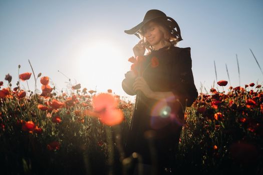 a girl in a black dress and hat on a poppy field at sunset
