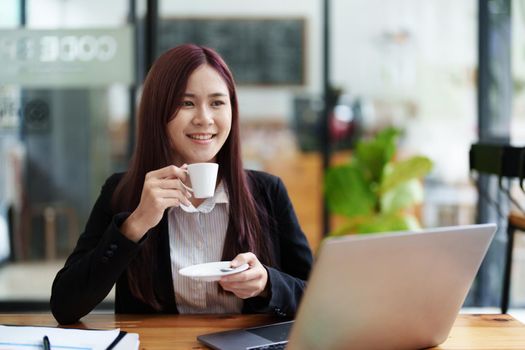 Asian business woman drinking coffee and using computer in office