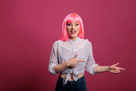 Carefree happy adult with pink hair pointing sideways in studio