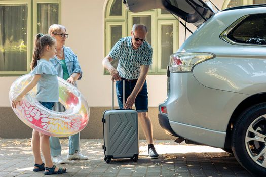 Elderly couple and niece loading baggage in trunk
