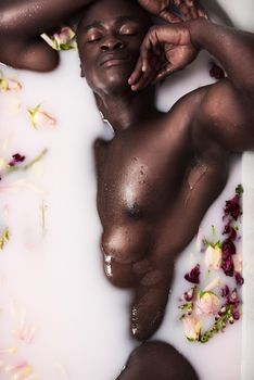 If youre going to bath go all out. a muscular young man having a milky bath filled with flowers at home.