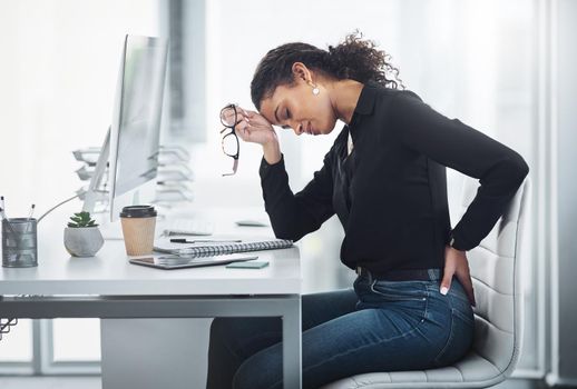 My back pain is just adding to my stress. a young businesswoman suffering with back ache in an office.