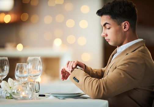 Am I being stood up. a handsome young man checking his watch while sitting in a fancy restaurant.