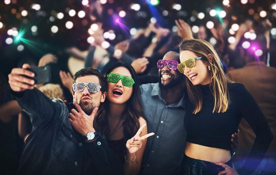 These fancy glasses deserve to be remembered. a diverse group of young friends taking a selfie together at a party at night.
