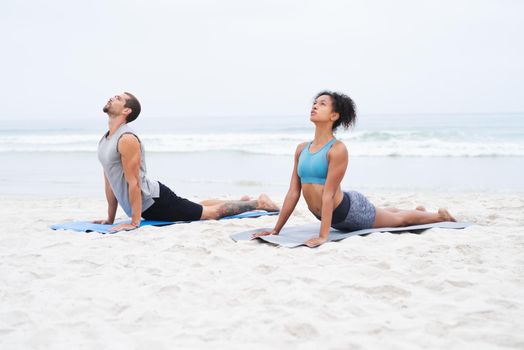 Let the calm air fill your mind and body. a young man and woman practising yoga together at the beach.