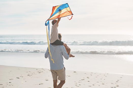 This kite needs to take off. Rearview shot of a young boy being carried on his fathers shoulders and holding a kite on the beach.