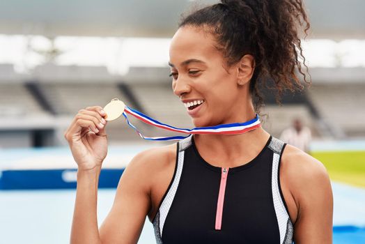 The glory of the gold. an attractive young female athlete posing with her gold medal out on the track.