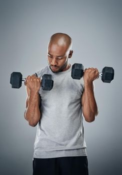 Work on a stronger and you. a sporty young man working out with weights against a grey background.
