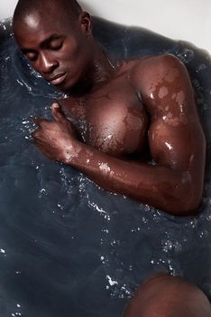 Wash away the dark days of yesterday. a handsome young man submerged in a bath filled with dark water.