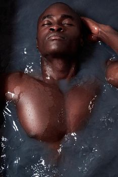 Take your stress to the tub. a handsome young man submerged in a bath filled with dark water.