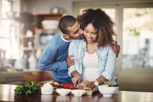 Romantic, loving and caring boyfriend embraces his girlfriend and shows affection while they make food in the kitchen. A couple sharing a kiss and hug while cooking a meal or salad at home.