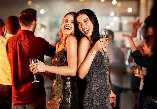 Back to back. two cheerful young women having drinks while dancing on the dance floor of a club at night.