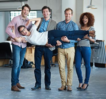 Colleagues having fun, playing and feeling playful while carrying fun coworker, being silly and goofy in office together. Portrait of diverse group or team of smiling creative business men and women