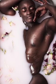 Your body is a reflection of how you treat it. a muscular young man having a milky bath filled with flowers at home.