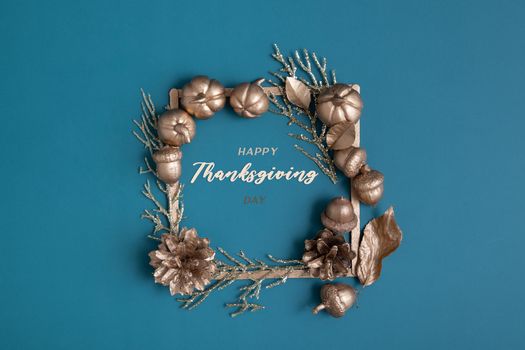 Happy Thanksgiving lettering with flat lay golden pumpkins and acorns on a turquoise background