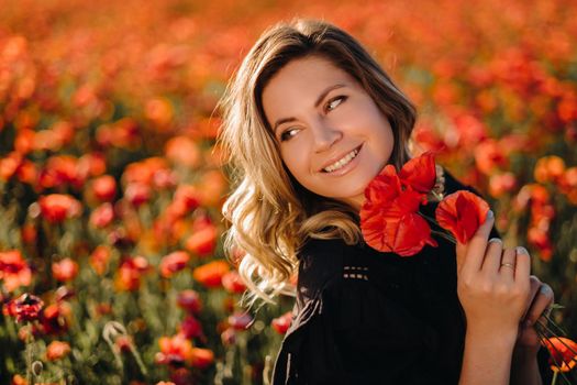 a girl in a black dress on a poppy field at sunset