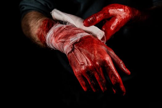 A man covered in blood bandages his hands.