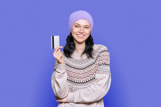 Young beautiful teenage female with credit card on purple background