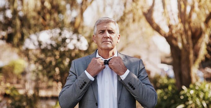 He knows the importance of a perfect necktie. Cropped portrait of a handsome mature bridegroom adjusting his necktie while preparing for his wedding outdoors.