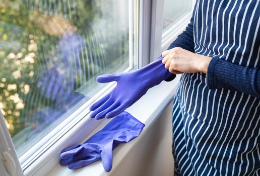 A young girl in a striped apron puts purple gloves on her hands. To prepare for washing windows in an apartment or house. Cleaning and cleaning concept.