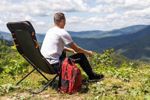 idyllic and rural scene. A man chilling and resting after hiking sitting on a chair and looking in the mountains