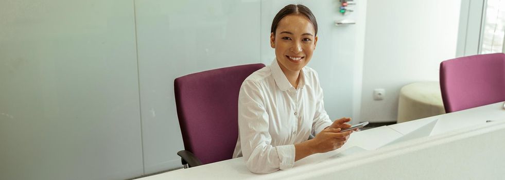 Smiling asian business woman sitting in meeting room and holding phone