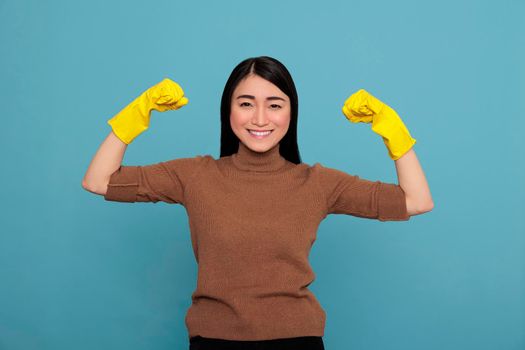 Happy energetic beautiful asian housewife raising arms and showing biceps