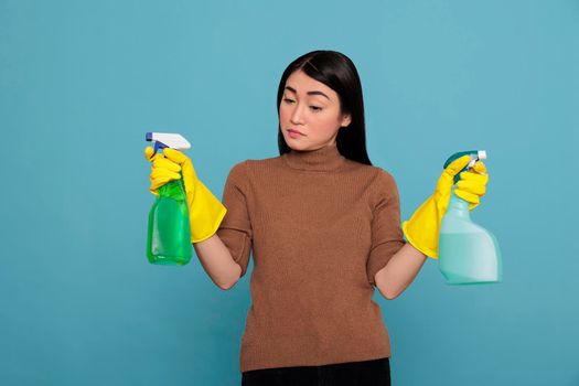Portrait of pretty sad asian woman holding two detergent sprays