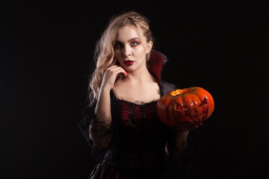 Portrait of beautiful vampire woman with halloween pumpkin