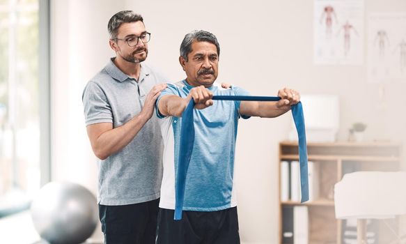 Growing stronger with every stretch. a senior man exercising with a resistance band during a rehabilitation session with his physiotherapist.