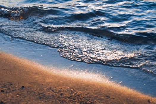 Blue sea waves and golden sand in sunshine glow at sunset, sandy beach and coastal nature