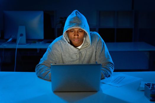 Hacking away in the late hours of the night. a young male hacker using a laptop in the dark.