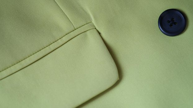 Closeup of green jacket with black button and pocket