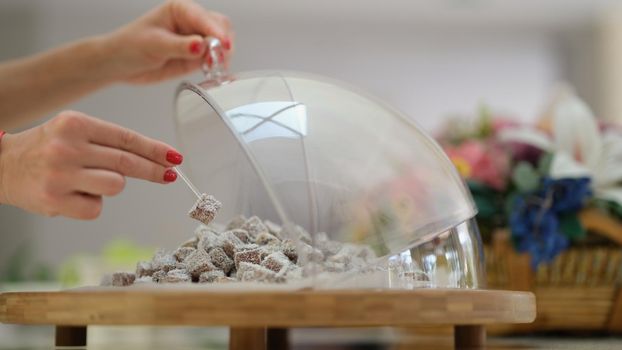 Woman hand takes piece of Turkish delight with coconut sprinkling from transparent dish closeup