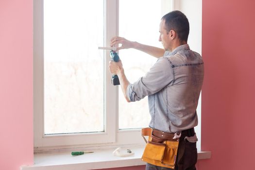 Handyman using a cordless screwdriver to install a window handle. Qualified worker services, home repair and renovation.