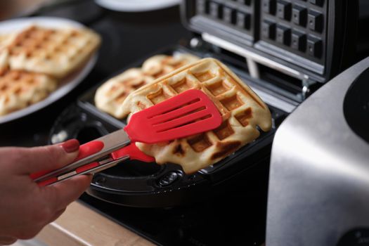 Pastry chef takes hot waffles from waffle iron in kitchen
