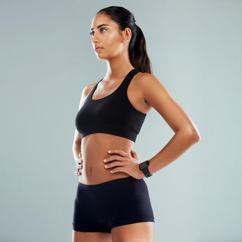 Her focus is unmatched. Studio shot of an athletic young woman posing with her hands on her hips against a grey background