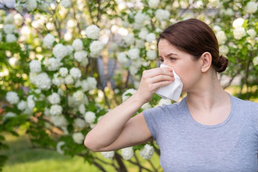 Middle-aged woman blowing her nose in a flowering garden.