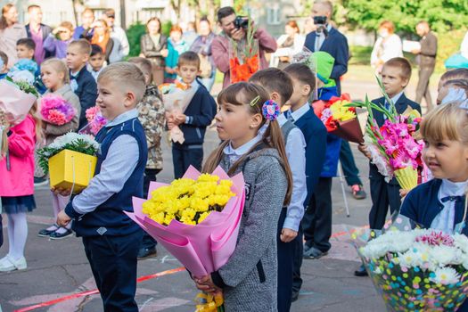 NOVOKUZNETSK, KEMEROVO REGION, RUSSIA - SEP, 1, 2021: Meeting with the first-grade pupils and teacher at schoolyard. The day of knowledge in Russia.
