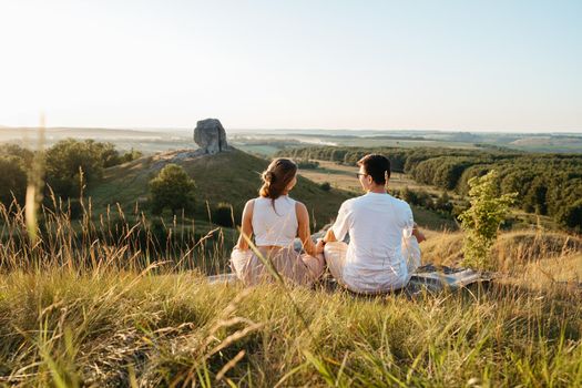 Man and Woman Practicing Yoga and Meditation Outdoors at Sunset with Scenic Landscape and Nature Miracle Giant Stone on the Background