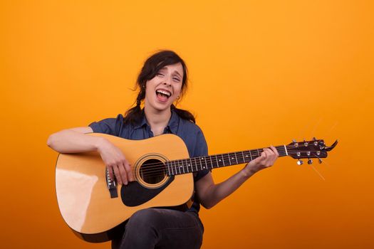 Portrait young singer with acustic guitar in studio over yellow background