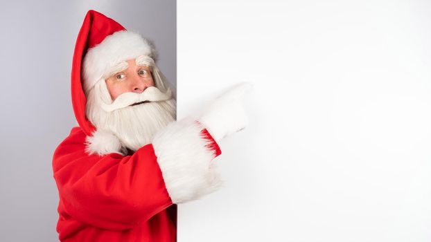 Santa Claus peeks out from behind an ad on a white background. Merry Christmas.