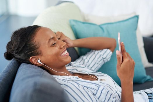 Plugged in to her weekend jams. a young woman wearing earphones while using a cellphone at home.