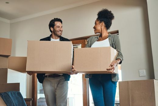 Happy couple or new home owners moving in together, carrying boxes of furniture or belongings and property. Loving, interracial partners after the purchase of real estate, smiling at each other.